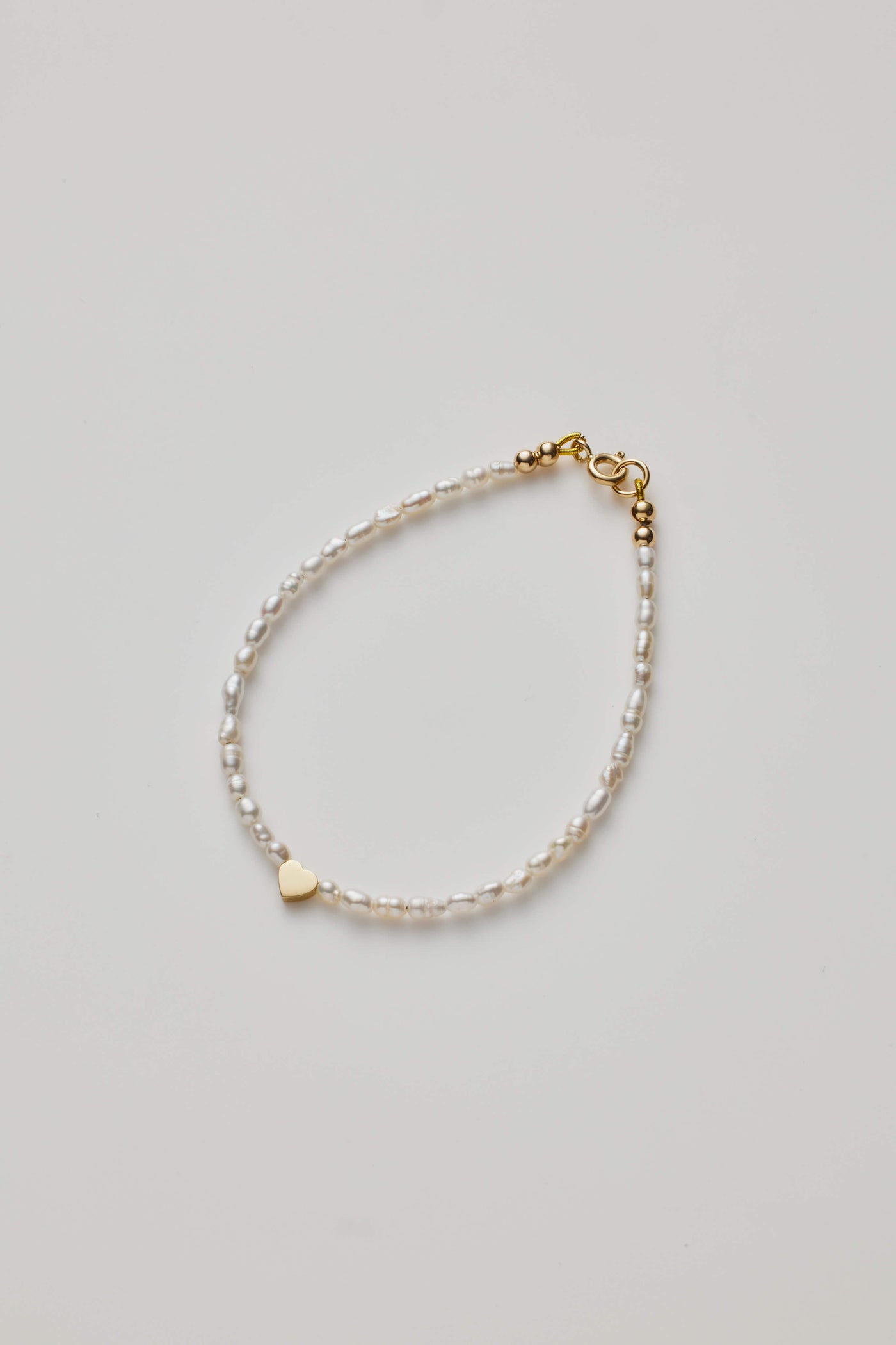 Delicate bracelet with lustrous pearls and a gold heart charm, elegantly crafted.