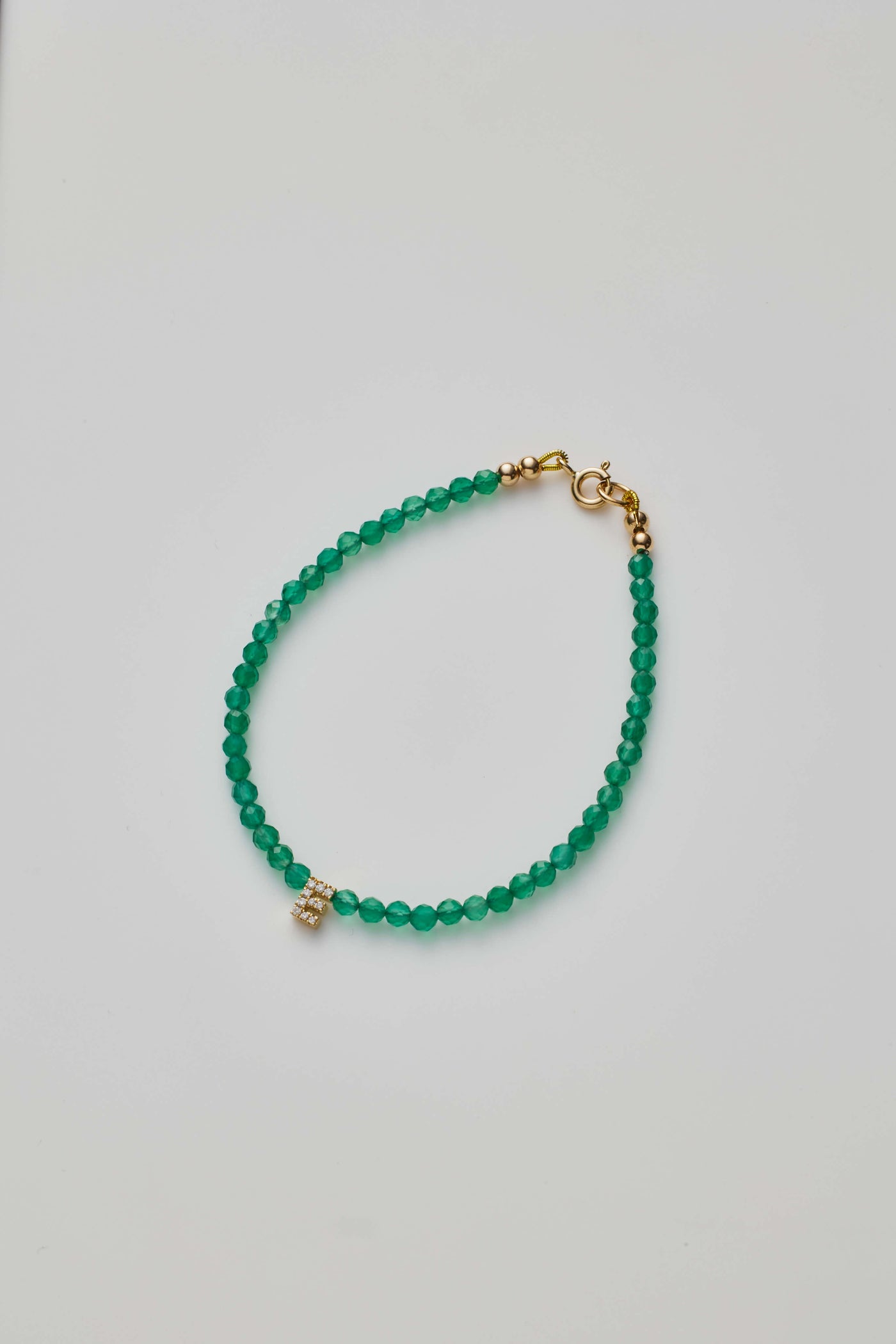 Delicate bracelet with green onyx beads and a diamond alphabet charm, elegantly crafted.