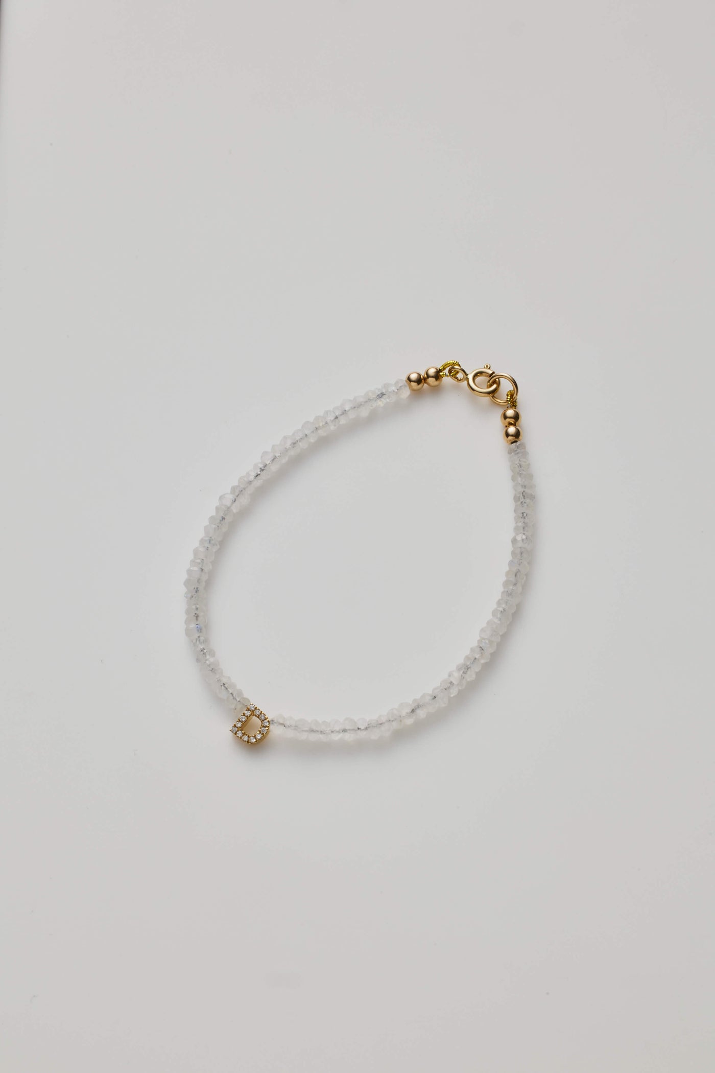 Delicate bracelet with moonstone beads and a diamond alphabet charm, elegantly crafted.