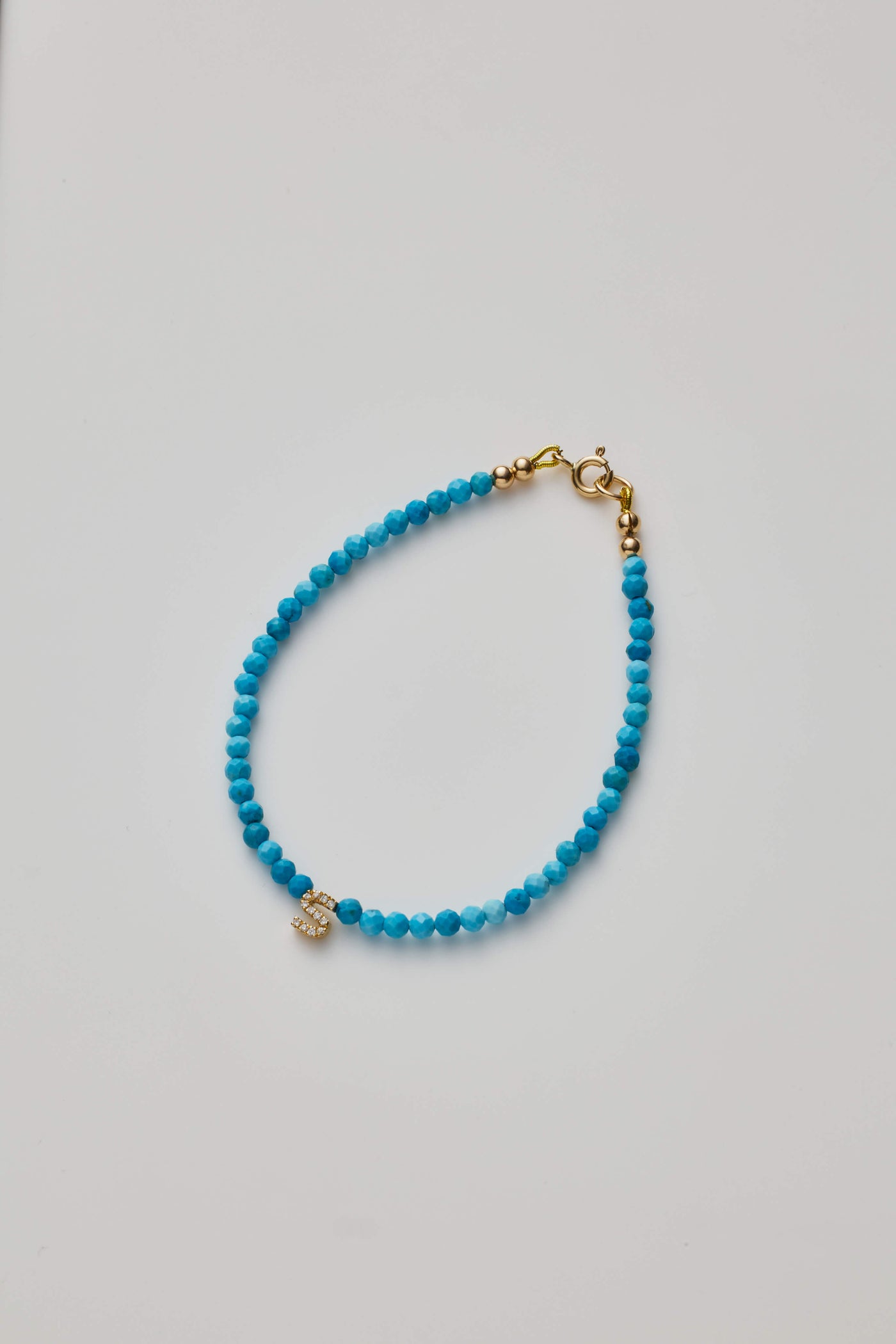 Delicate bracelet with Turquoise beads and a diamond alphabet charm, elegantly crafted.