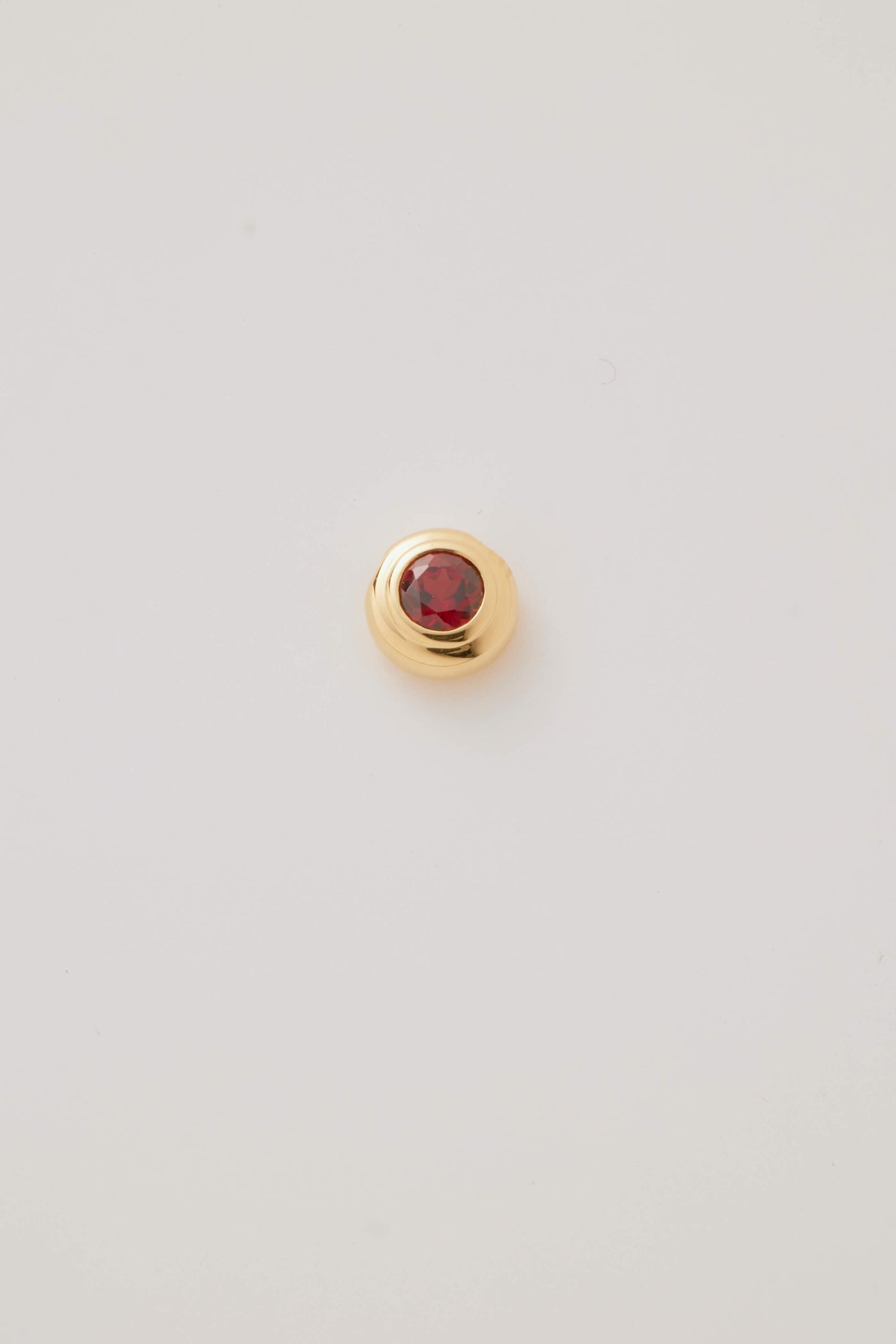 Close-up image of the January Birthstone Charm featuring a rich red garnet gemstone in a polished gold setting. 