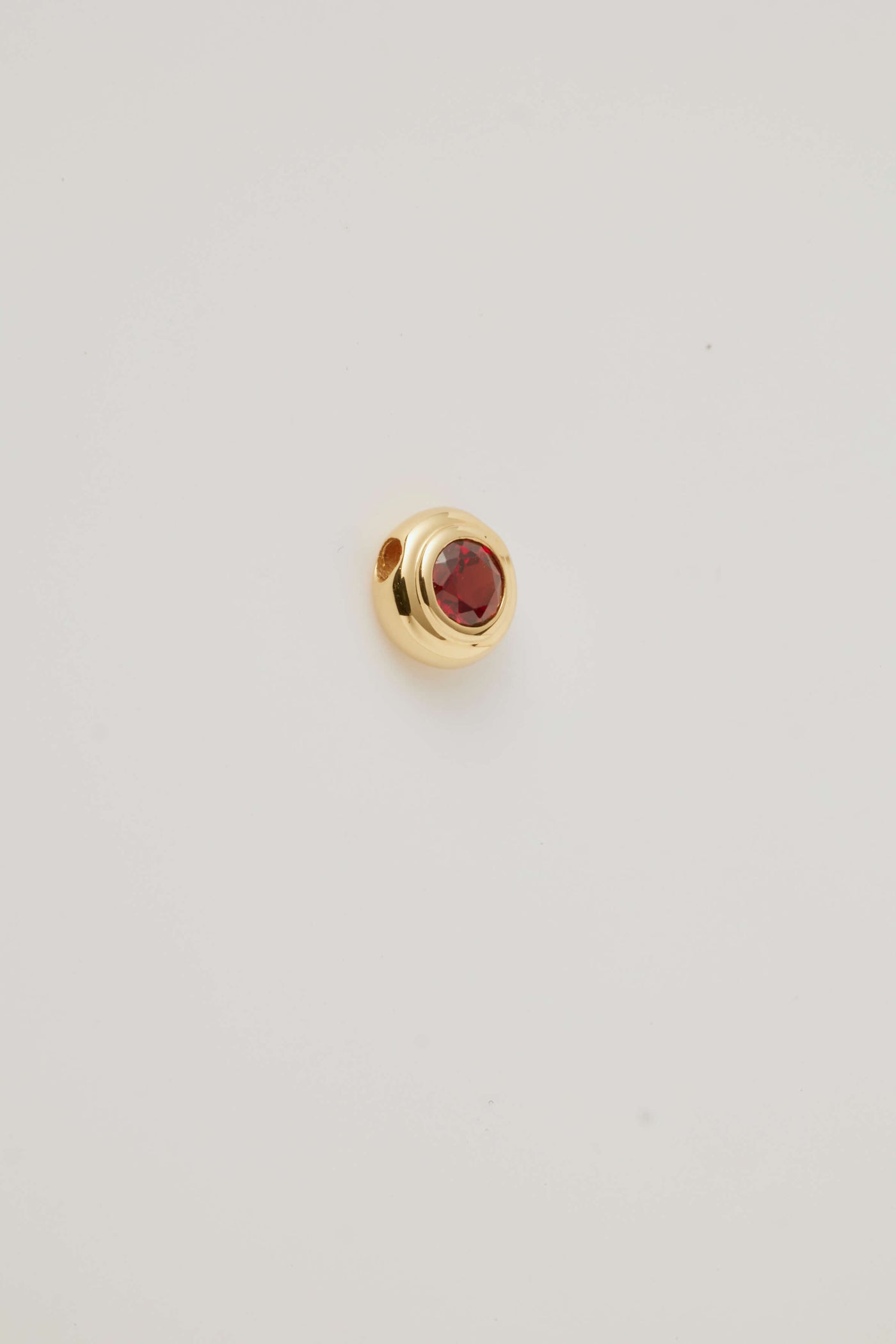 Side view image of the January Birthstone Charm featuring a rich red garnet gemstone in a polished gold setting. 