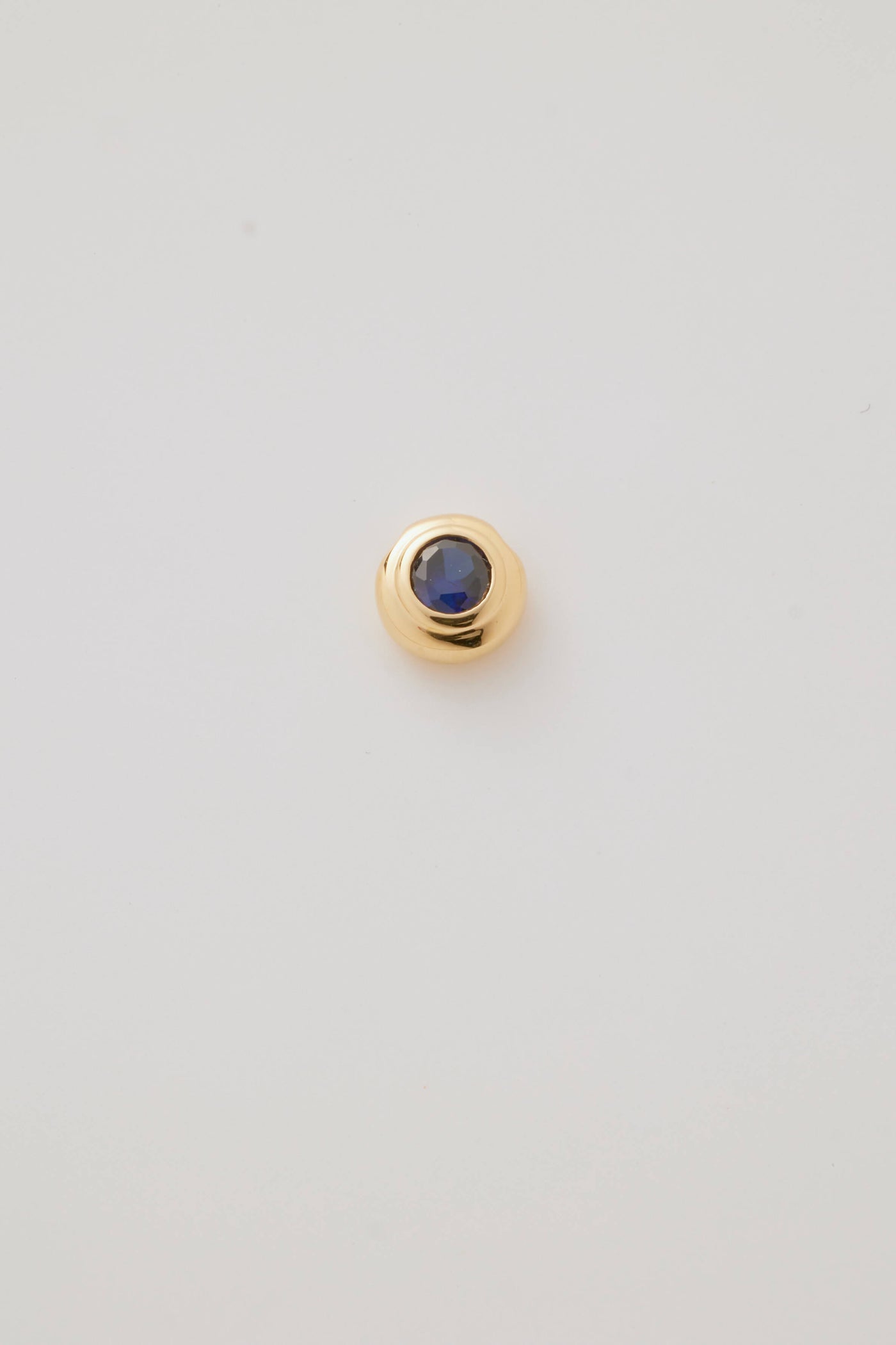 Close-up image of the September Birthstone Charm featuring a deep blue sapphire gemstone in an elegant gold setting. Photographed on a light grey background.