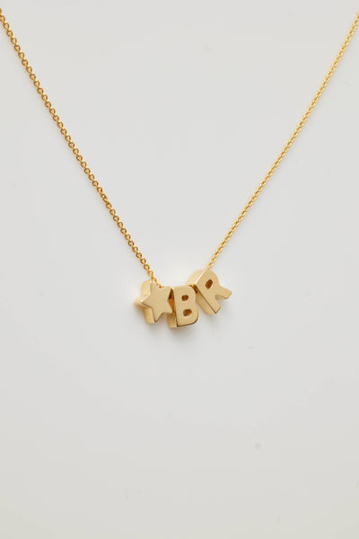 The Two Letters and Star Necklace in 18k Gold is a delicate piece featuring three charms: the letters "B" "R" separated by a small star, all suspended from a fine chain with an openable connector clasp. The plain white background highlights the simplicity and elegance of this exquisite necklace.