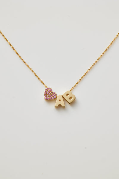 Introducing the "Two Letters and Pink Sapphire Heart Necklace in 18k Gold." This elegant gold necklace features customisable letter charms, a small pink sapphire heart, and the letters "A" and "B" with the heart preceding them. These charms dangle from a delicate and stylish 18k solid gold chain.