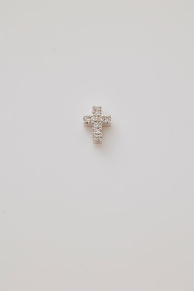 A radiant white gold cross charm adorned with sparkling diamonds photographed from above on a light grey background.