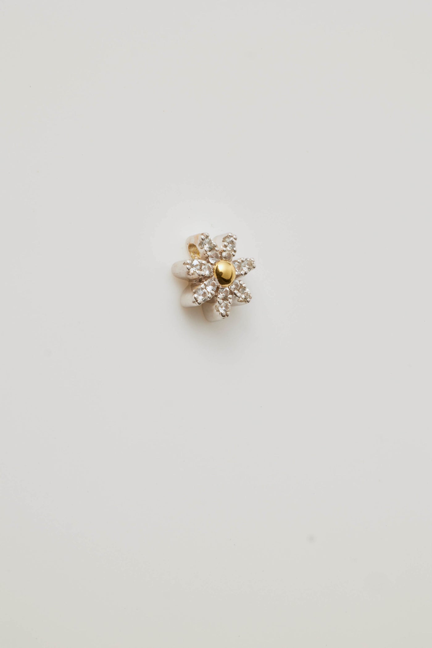 Side view profile of a sparkling diamond daisy charm featuring a radiant centre stone and petal-like diamonds. Elegantly photographed on a light grey background.