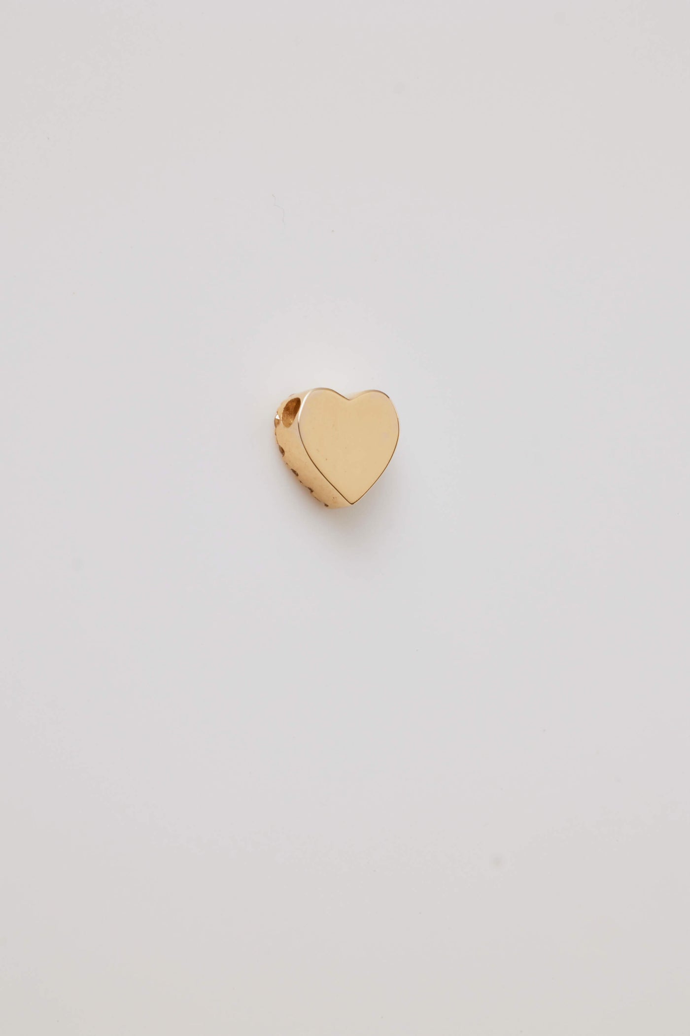 A close-up side view of the reverse side of a diamond-accented solid gold heart pendant. The heart's edges are smooth and polished, with a small opening at the top designed as a loop for a chain. The pendant's side profile highlights its depth and thickness, with the diamonds subtly encrusted along the heart's curve, adding sparkle and elegance.