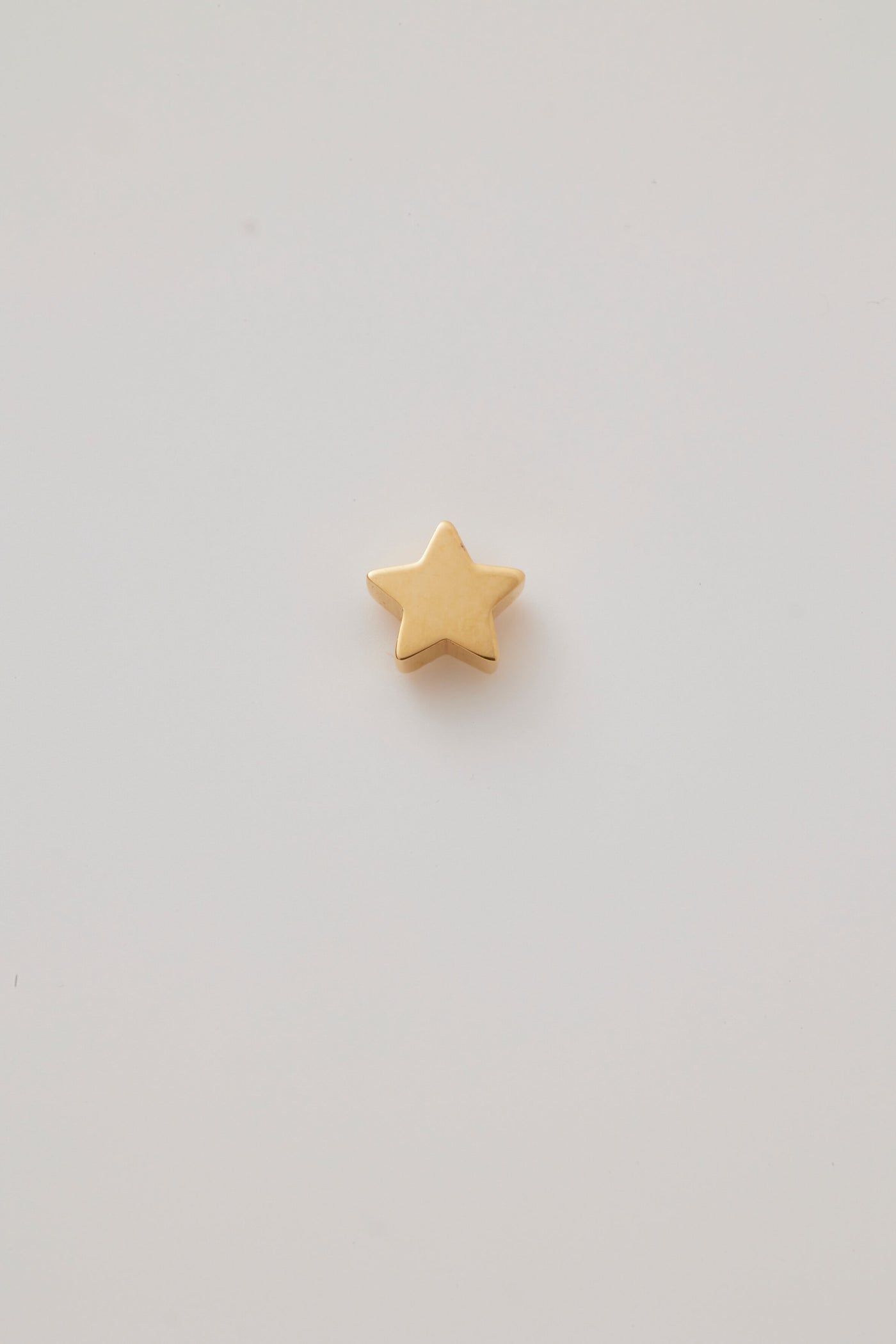 A solid gold star pendant with a smooth, polished surface, showcasing its clean lines and symmetrical five-pointed design. The pendant has a small hole at the top for attaching to thread a chain, through blending seamlessly with the star's sleek, shiny finish.