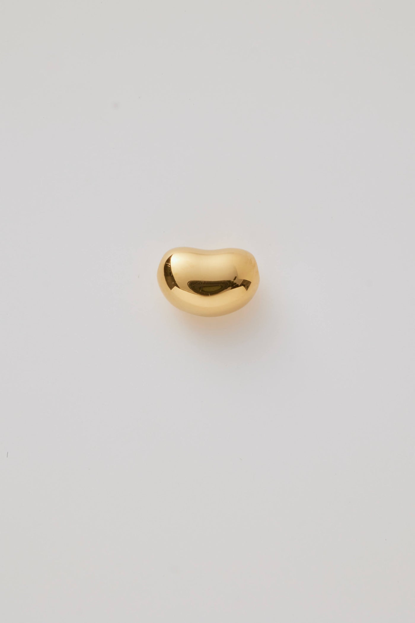 The reverse, back side of a small gold bean-shaped charm with a smooth, polished finish and hole through the centre for threading a necklace chain. 