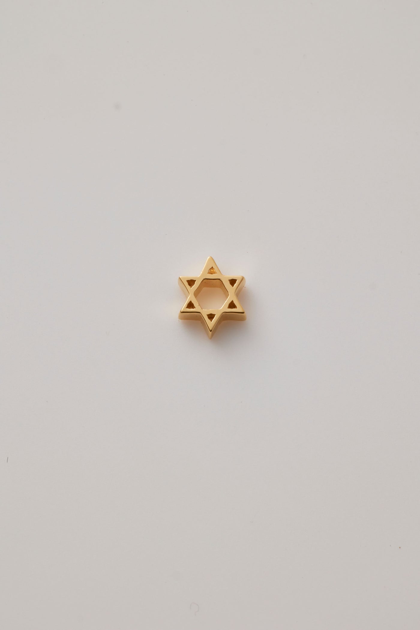 A beautifully crafted Star of David charm made from polished 18-karat gold with a sleek finish. The charm features two interlocking triangles creating the iconic six-pointed star, symbolizing unity and heritage. 