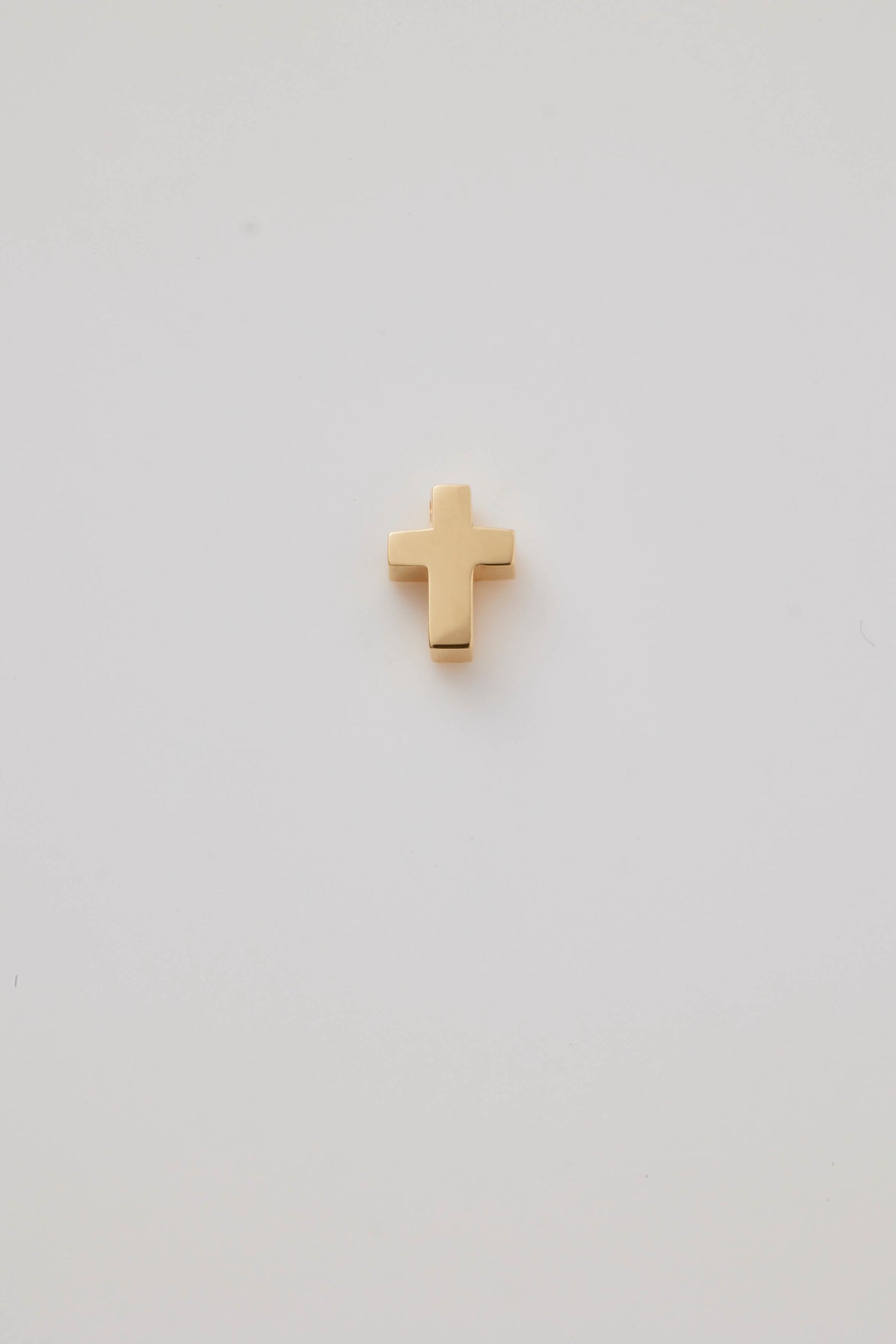 A delicate Christian cross charm crafted from polished 18-karat gold. The charm features clean, elegant lines with a smooth, shiny finish that reflects light beautifully. Its minimalist design emphasises simplicity and sophistication, making it a versatile accessory for both everyday wear and special occasions. The hole at the top allows easy chain threading a chain or bracelet.