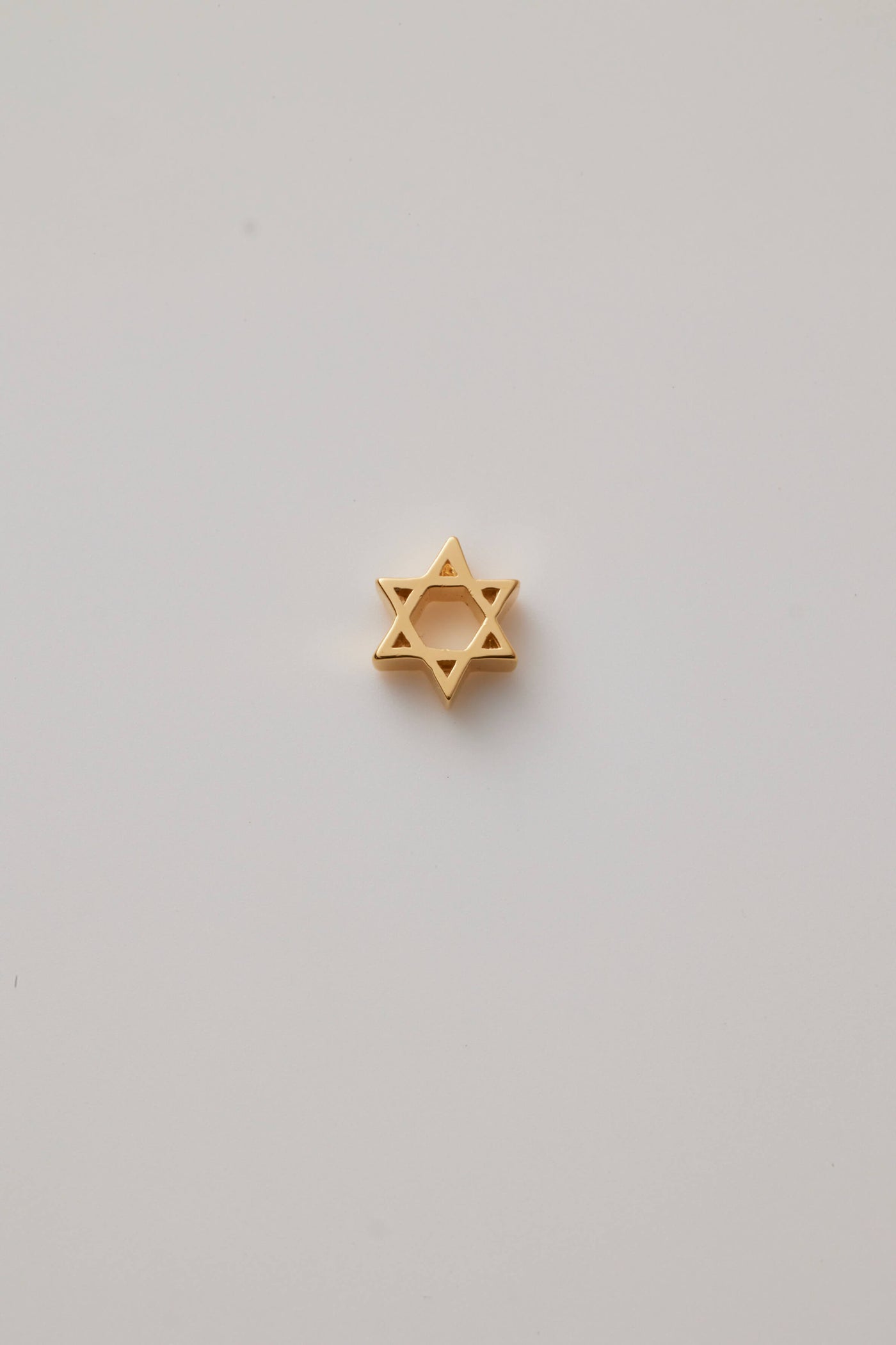 The reverse side of the Star of David charm is crafted from polished 18-karat gold with a sleek finish. This charm showcases two interlocking triangles that form the iconic six-pointed star, symbolizing unity and heritage.