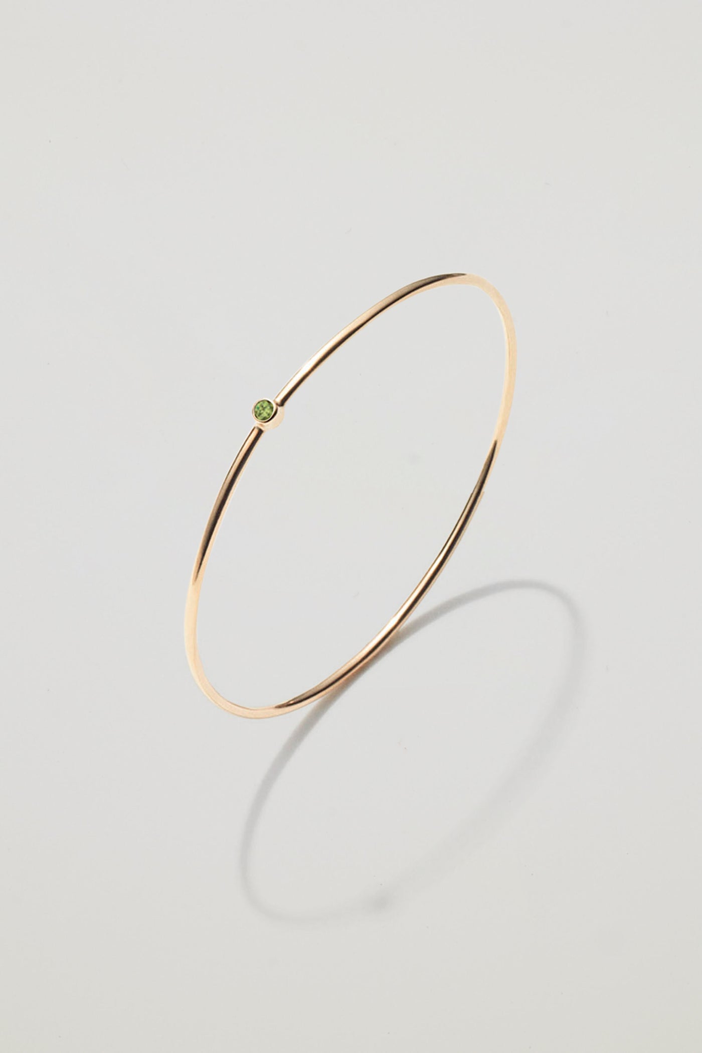Solid gold bangle with an August peridot birthstone, symbolising optimism and renewal.