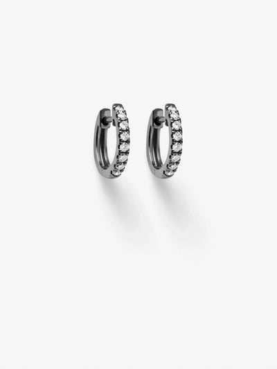 A pair of elegant, small huggie earrings are crafted in 18k blackened gold and encrusted with round brilliant diamonds. They are displayed side by side against a plain white background, casting a slight shadow. The simple, symmetrical design makes them suitable for various occasions.