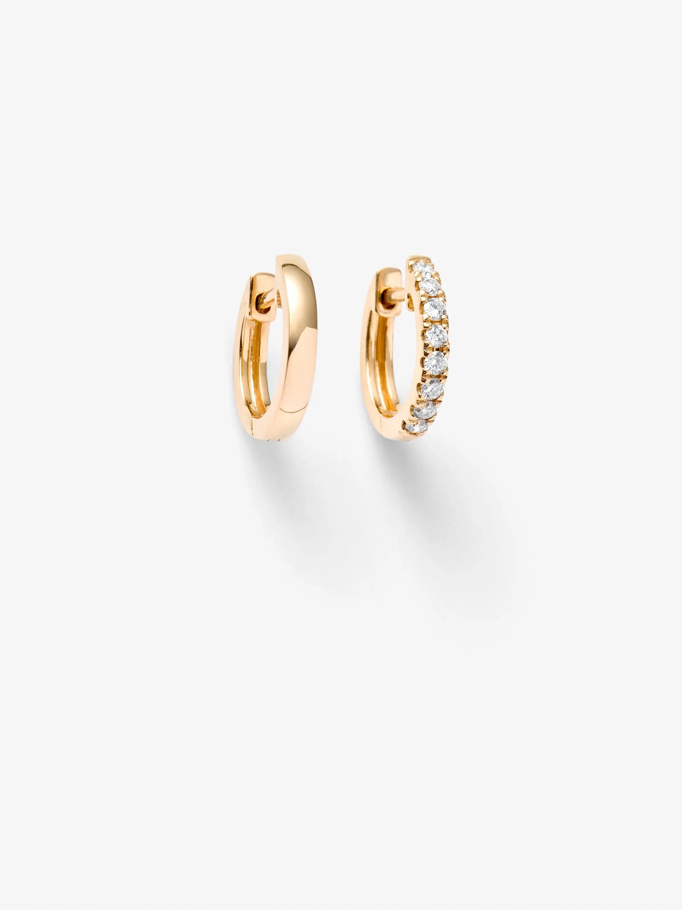 The Huggie Earrings in Diamonds and 18k Gold are displayed against a white background. The earring on the right is adorned with round brilliant diamonds along the outer edge, while the earring on the left has a smooth, polished finish.