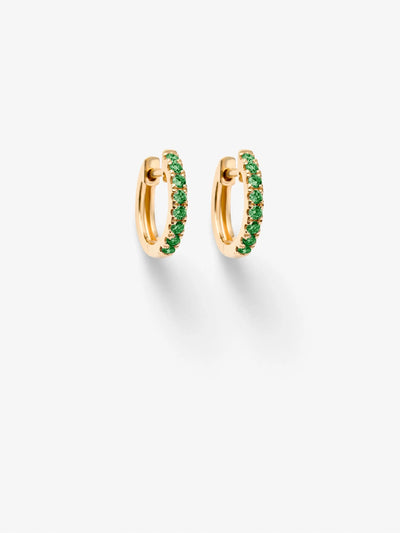 Image shows a pair of Huggie Earrings in Tsavorite and 18k Gold. These small, elegant hoops are adorned with a row of green tsavorite gemstones, offering a simple yet sophisticated design. The gemstones add a touch of color and sparkle. The earrings are positioned against a white background, casting subtle shadows.