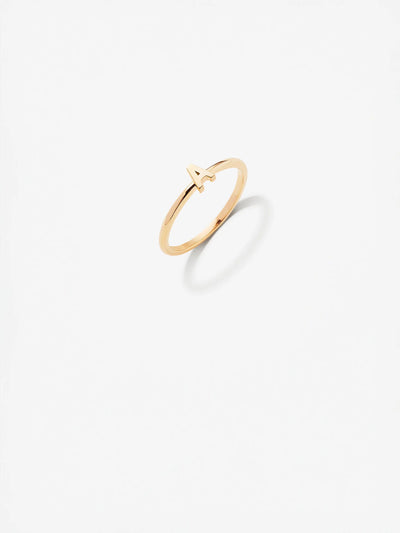 The Letter A Ring in 18k Gold is a delicate, custom-made piece with a minimalistic design that features a small, stylized "A" on top. The 18k solid gold ring casts a soft shadow on a plain white background.