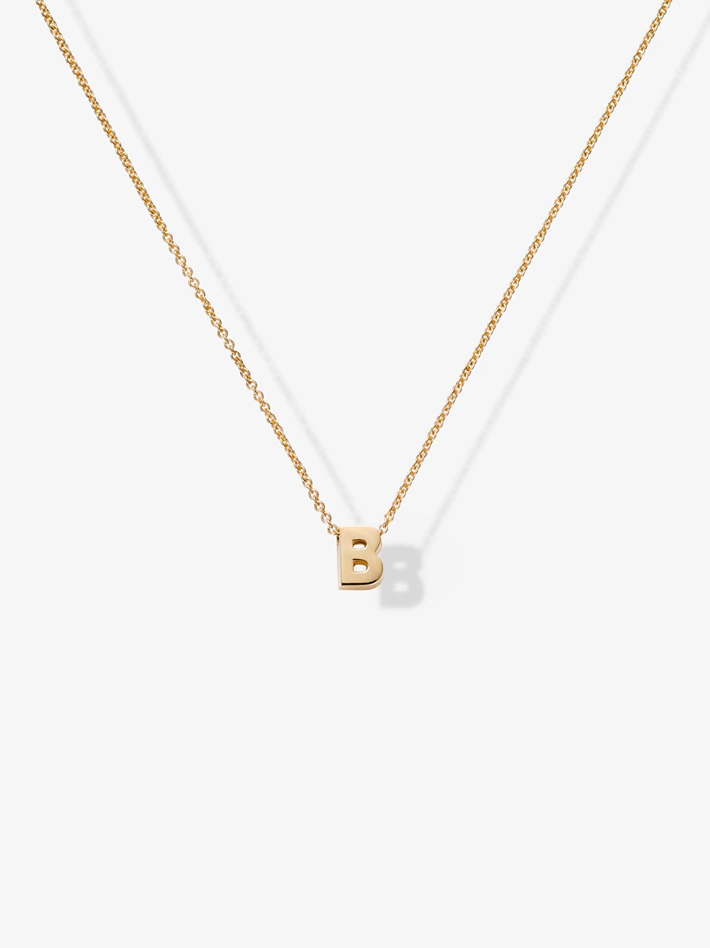 The Letter B Necklace in 18k Gold features a delicate chain and a small, simple pendant in the shape of the letter "B," elegantly displayed on a white background.