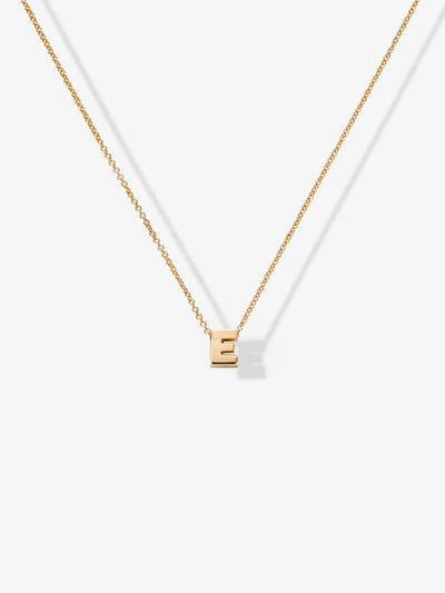 The Letter E Necklace in 18k Gold boasts a fine chain and a small pendant shaped like the letter "E," meticulously crafted from signature 18k gold chains and set against a pristine white background.