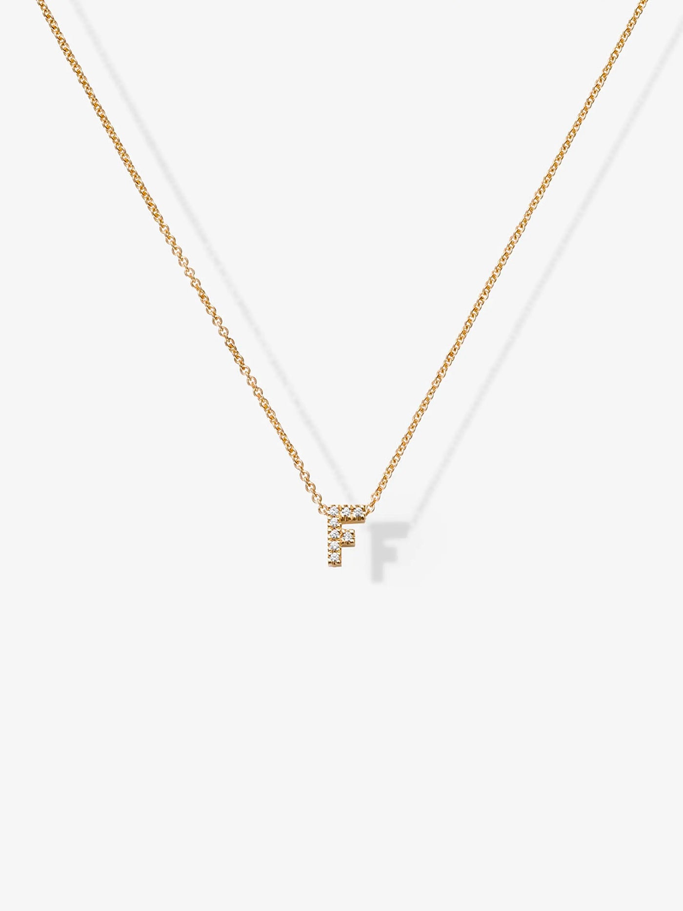 The Letter F Necklace in Diamonds and 18k Gold features a delicate 18k gold chain adorned with a small, sparkling "F" pendant. The letter "F" is encrusted with tiny diamonds, adding an elegant touch to this personalized piece of jewelry, which is beautifully displayed against a plain white background.