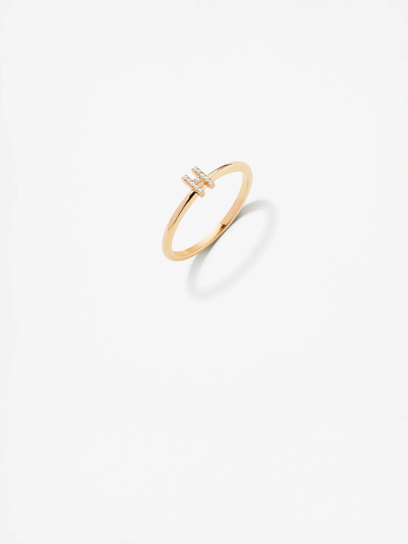 The Letter H Ring in Diamonds and 18k Gold is displayed on a white background. This minimalist 18k solid gold ring features a simple band with a small, vertical bar adorned with tiny diamonds at the center, perfect for stacking rings or combining with other letter rings to create a personalized look.