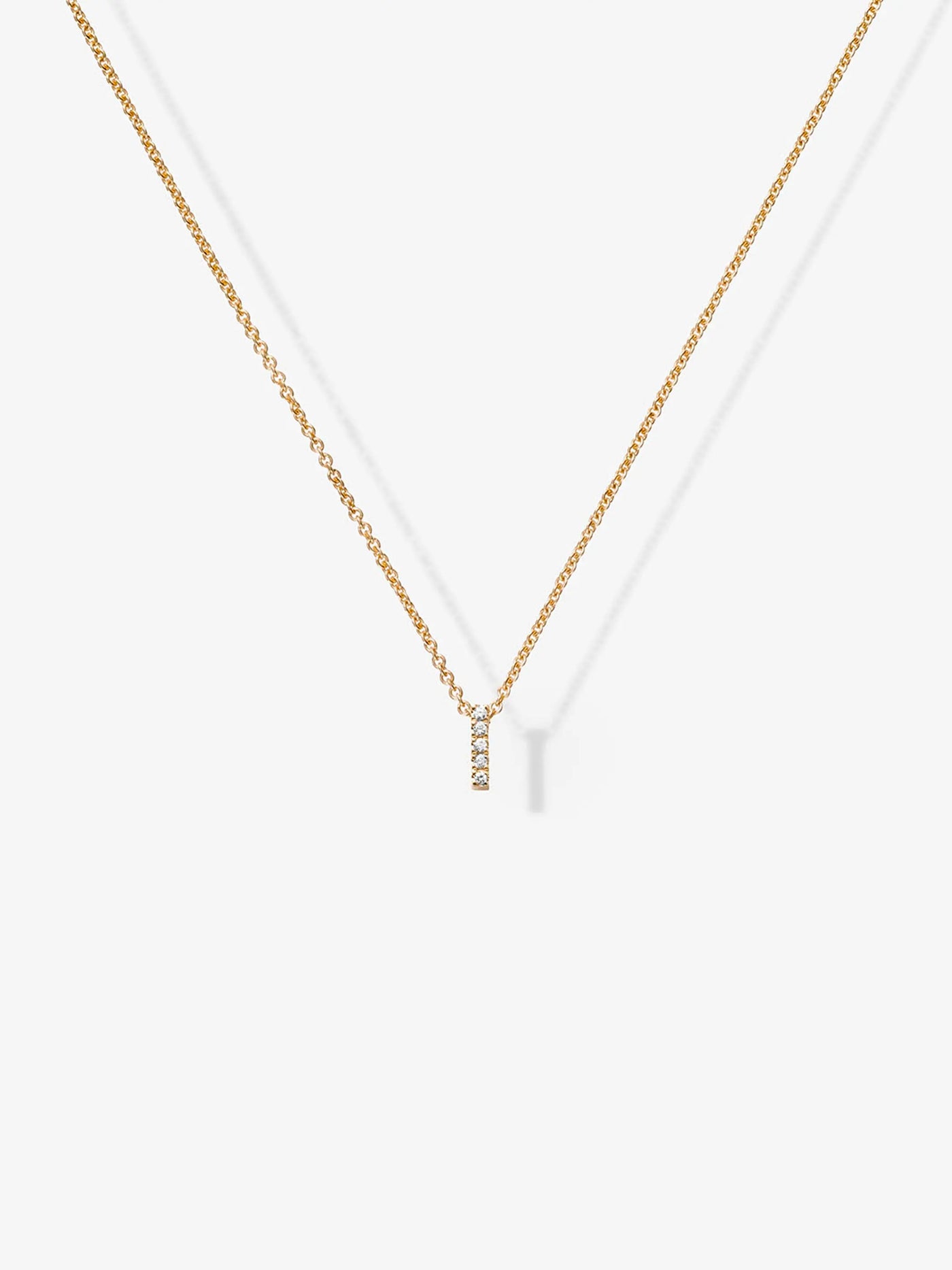 The Letter I Necklace in Diamonds and 18k Gold features a delicate 18k solid gold chain with a small vertical 'I' pendant. The necklace is displayed against a plain white background, showcasing its minimalist design enhanced by the diamonds or small gemstones encrusted on the pendant, adding a subtle touch of sparkle.