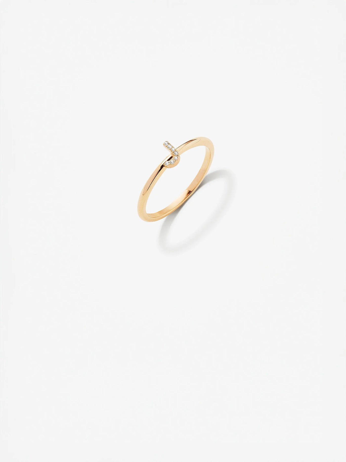 The Letter J Ring in Diamonds and 18k Gold is a delicate, custom-made piece featuring a sleek, minimalist design. The 18k gold band is simple and smooth, adorned with a tiny, sparkling diamond accent shaped like the letter "J." Against the white background, the ring casts a slight shadow that highlights its elegant and understated aesthetic.