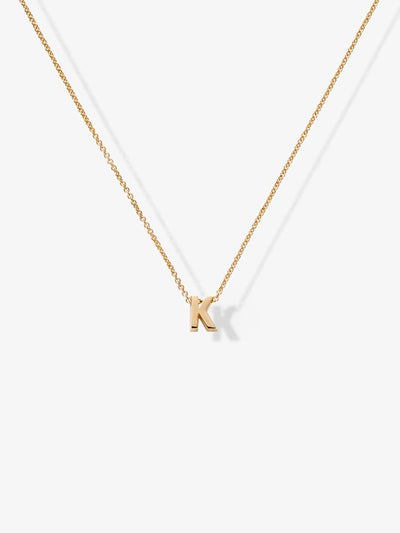 The Letter K Necklace in 18k Gold showcases a fragile chain adorned with a singular gold letter "K" pendant, elegantly presented against a pristine white background.