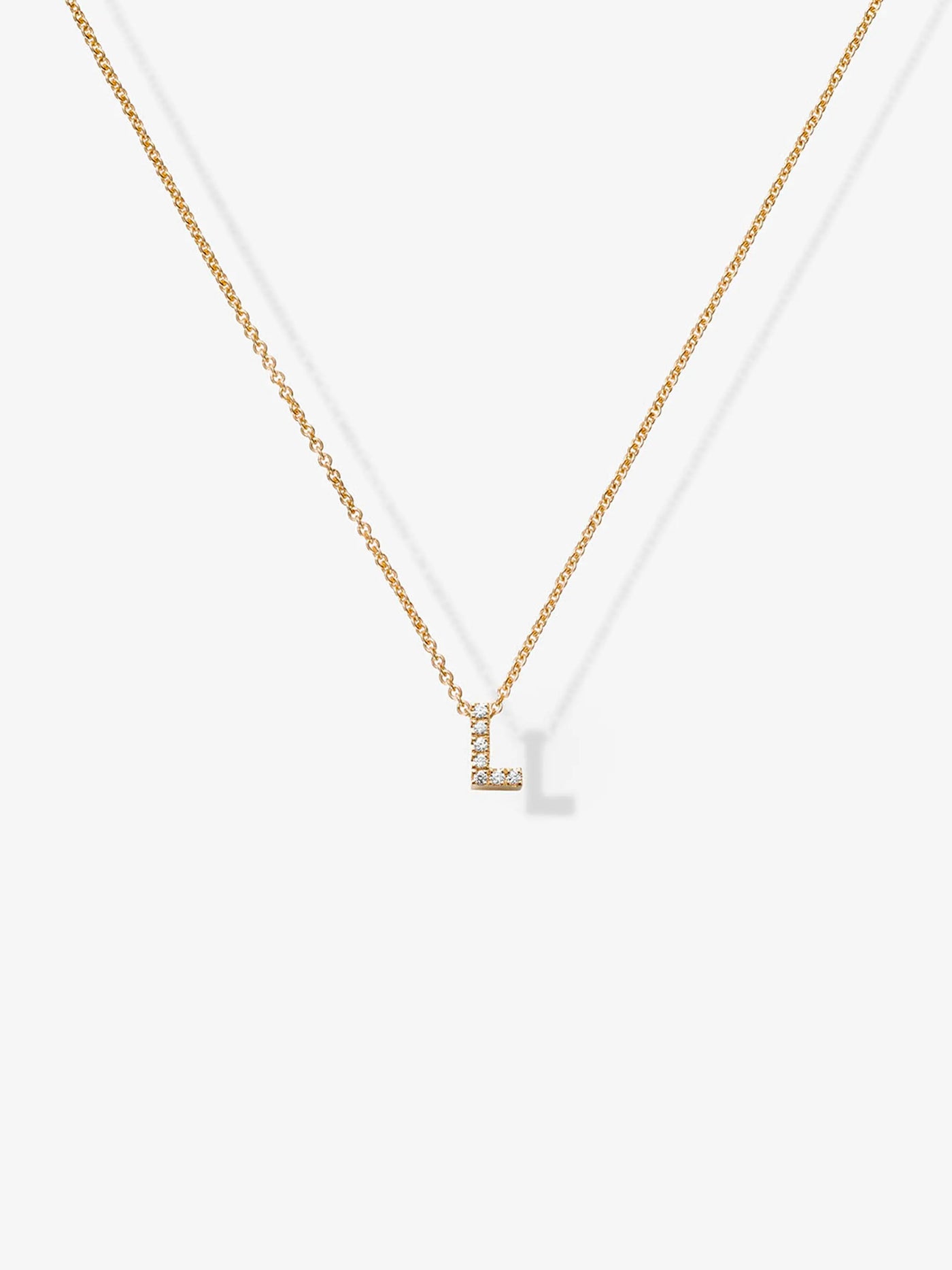 The Letter L Necklace in Diamonds and 18k Gold is a delicate piece featuring a small pendant shaped like the letter "L" encrusted with tiny crystals. This customizable charm necklace hangs from a thin gold chain against a plain white background.