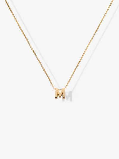 Introducing the Letter M Necklace in 18k Gold: a delicate chain necklace adorned with a single, elegant gold letter "M" pendant. The pendant is perfectly centered and suspended from the thin, sophisticated chain, creating a stunning contrast against a plain white background.