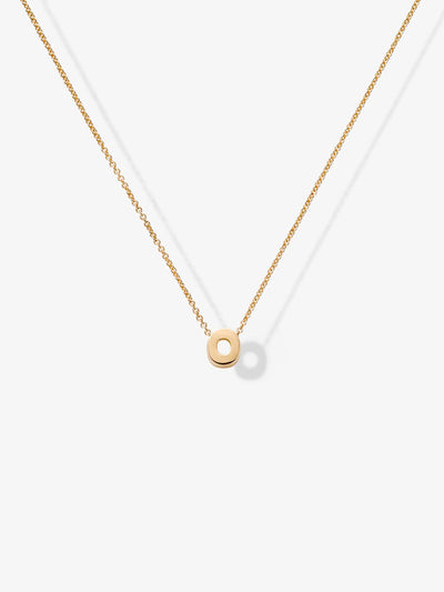 The Letter O Necklace in 18k Gold showcases a delicate chain and a small, circular pendant with a cut-out center. The charm hangs symmetrically in the middle of the chain against a plain white background.