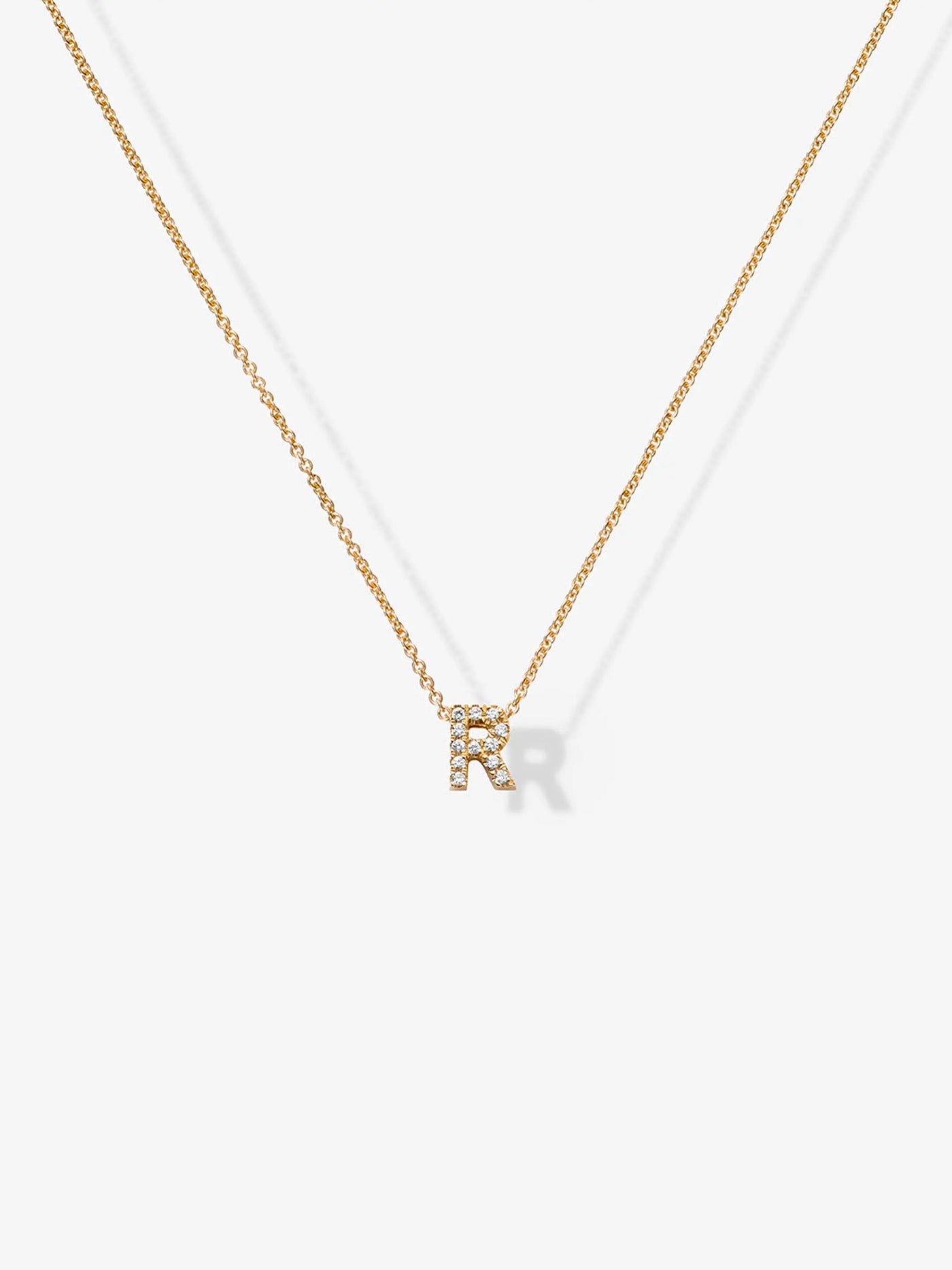 A delicate Letter R Necklace in Diamonds and 18k Gold features a pendant in the shape of the letter "R," adorned with small sparkling gemstones, and is shown against a plain white background.