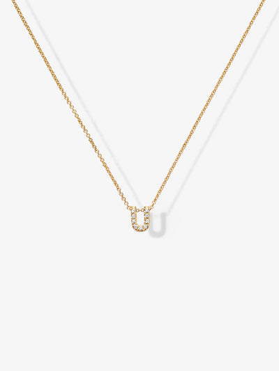 Introducing the Letter U Necklace in Diamonds and 18k Gold: A delicate 18k gold necklace featuring a small, horseshoe-shaped pendant adorned with tiny diamonds. The customizable gold chain is set against a plain white background, casting a faint shadow.