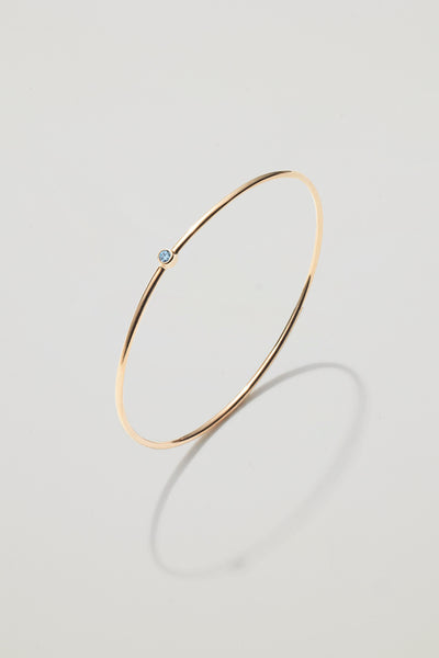 Solid gold bangle with a March aquamarine birthstone, symbolising renewal and courage.