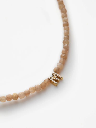 A close-up image of the One Letter Bracelet featuring blush moonstone beads. The bracelet is adorned with an 18k solid gold clasp, embellished with small, sparkling diamonds. The white background helps to highlight the intricate details of this elegant piece.