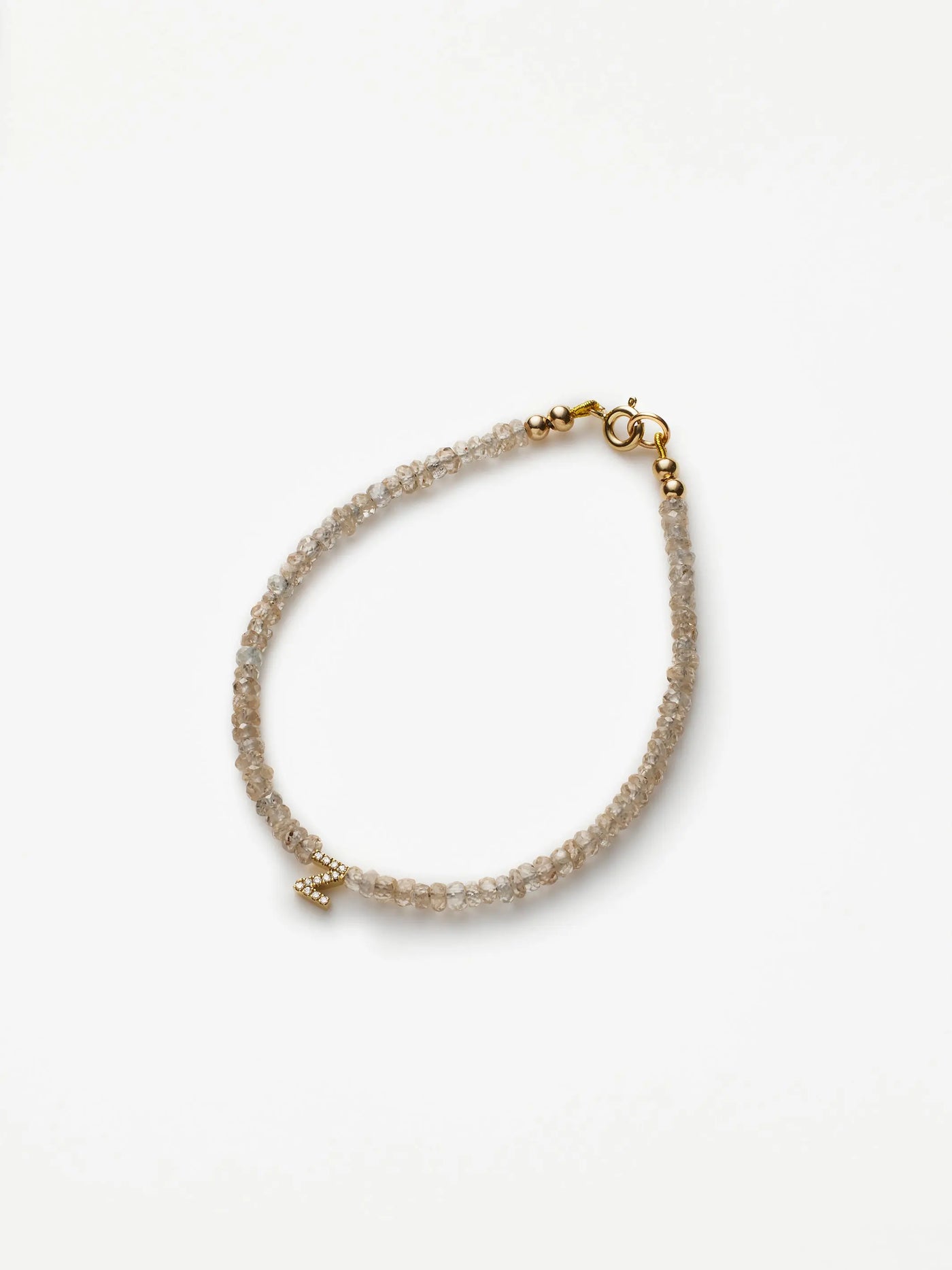 This One Letter Bracelet in Diamonds, Zircon and 18k Gold features a delicate dual-strand design of small, translucent beads connected by an 18k gold clasp. A small cross charm adorned with tiny crystals adds a subtle touch of elegance to the overall appearance. It is displayed on a plain white background.