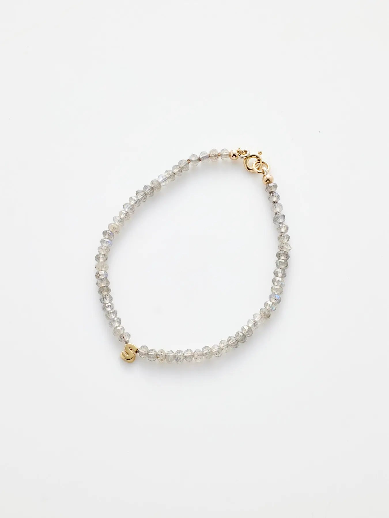 Image of the "One Letter Bracelet in Labradorite and 18k Gold," showcasing small, round, translucent beads strung together. The bracelet is secured with an 18k gold clasp and features a small gold initial charm near the clasp, symbolizing spiritual growth. The background is a clean, plain white.