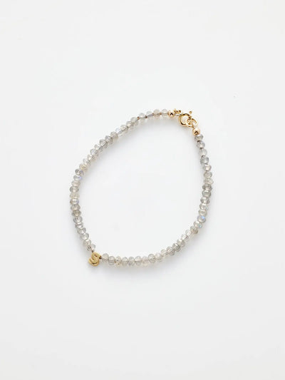 Image of the "One Letter Bracelet in Labradorite and 18k Gold," showcasing small, round, translucent beads strung together. The bracelet is secured with an 18k gold clasp and features a small gold initial charm near the clasp, symbolizing spiritual growth. The background is a clean, plain white.