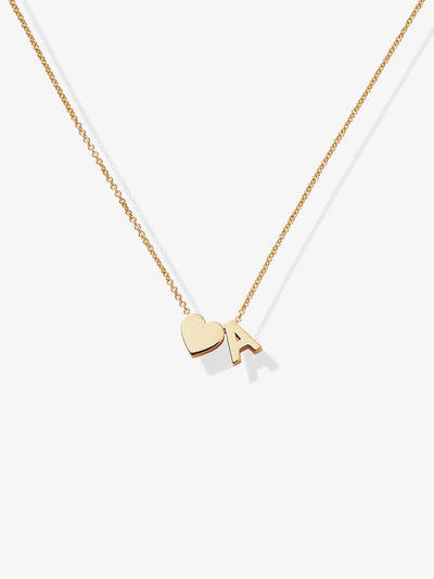 The One Letter and Heart Necklace in 18k Gold features a delicate solid gold chain adorned with two pendants: a heart and an "A". The heart and letter contribute to a simple, elegant design against a white background, exuding timeless charm.