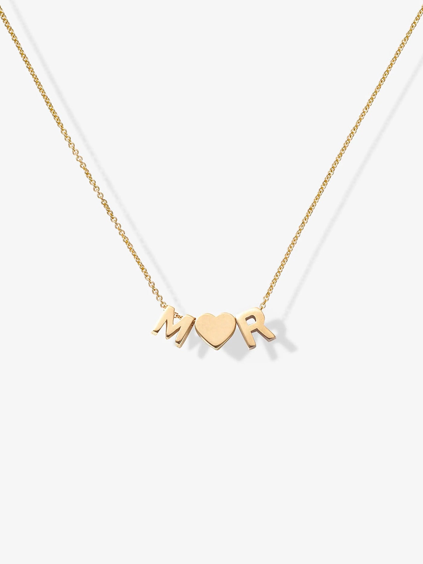 The Two Letters and Heart Necklace in 18k Gold boasts a delicate chain adorned with three exquisite charms: a capital letter "M," a heart symbol centrally placed, and a capital letter "R." Made from 18k solid gold, this beautiful piece is displayed against a simple, light-colored backdrop and features an openable connector clasp for effortless wear.