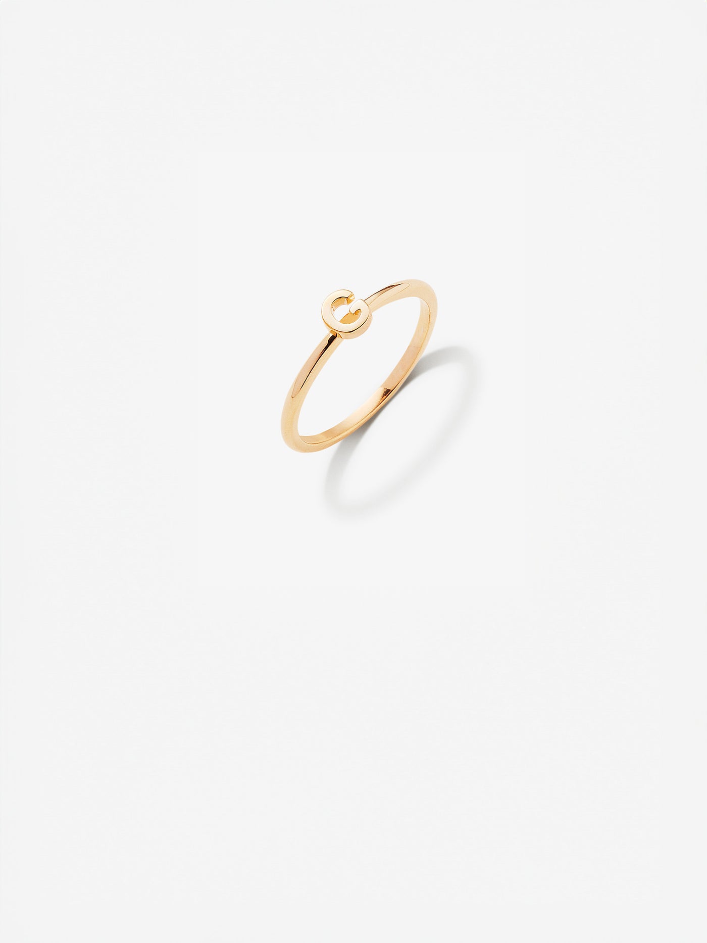 Close-up image of a personalised G gold ring adorned with intricate, miniature dimensional letters from the alphabet on a light grey background 