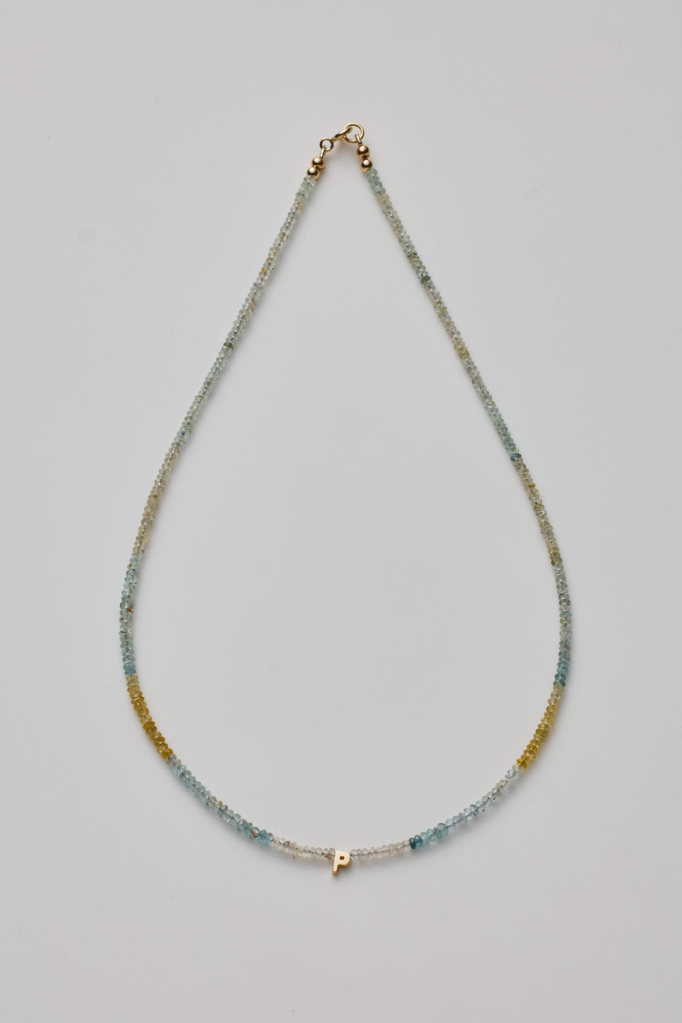 14K gold letter P necklace strung with naturally shaded aquamarine gemstones, showcasing ocean-inspired hues.