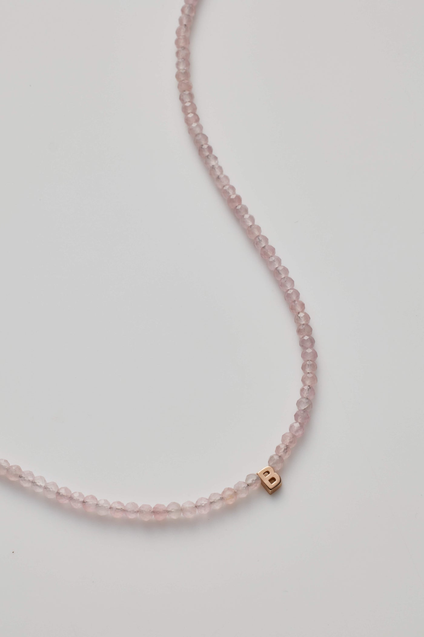 14K gold necklace with rose quartz crystal and a gold letter charm.